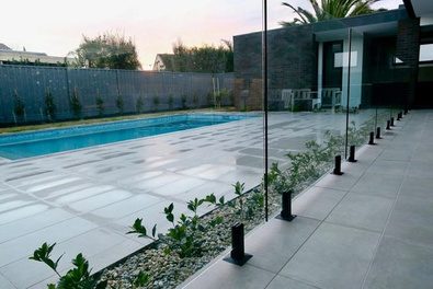 Glass pool fence with black spigots along a garden bed