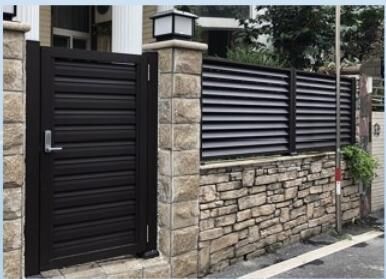 Black pedestrian gate beside a slat fence on a stone wall